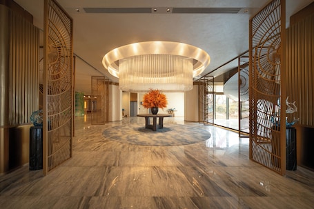 A lobby with a marble floor, a central table with a vase, and a large circular light fixture.. Grand Mercure Rizhao Haiqu