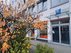 Una entrada de hotel con mostrador de recepción, un letrero que dice 'ibis budget hotels' y un edificio de fachada blanca.