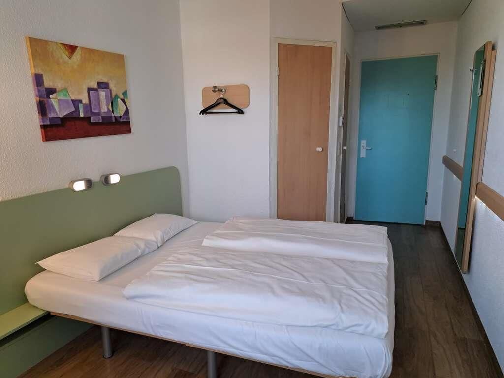 A room with a bed, a painting on the wall, a door, and a hallway.