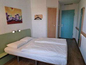 Una habitación con cama, un cuadro en la pared, una puerta y un pasillo.