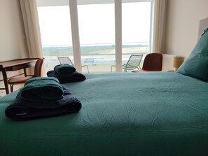 Una camera d'albergo con un letto grande, due poltrone, una scrivania e vista sulla spiaggia.