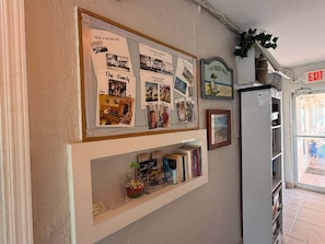 Eine Wand mit einem gerahmten Foto-Collage von Familienfotos, eine kleine Bücherablage mit Büchern und ein Schild mit der Aufschrift 'Our Beach House'.