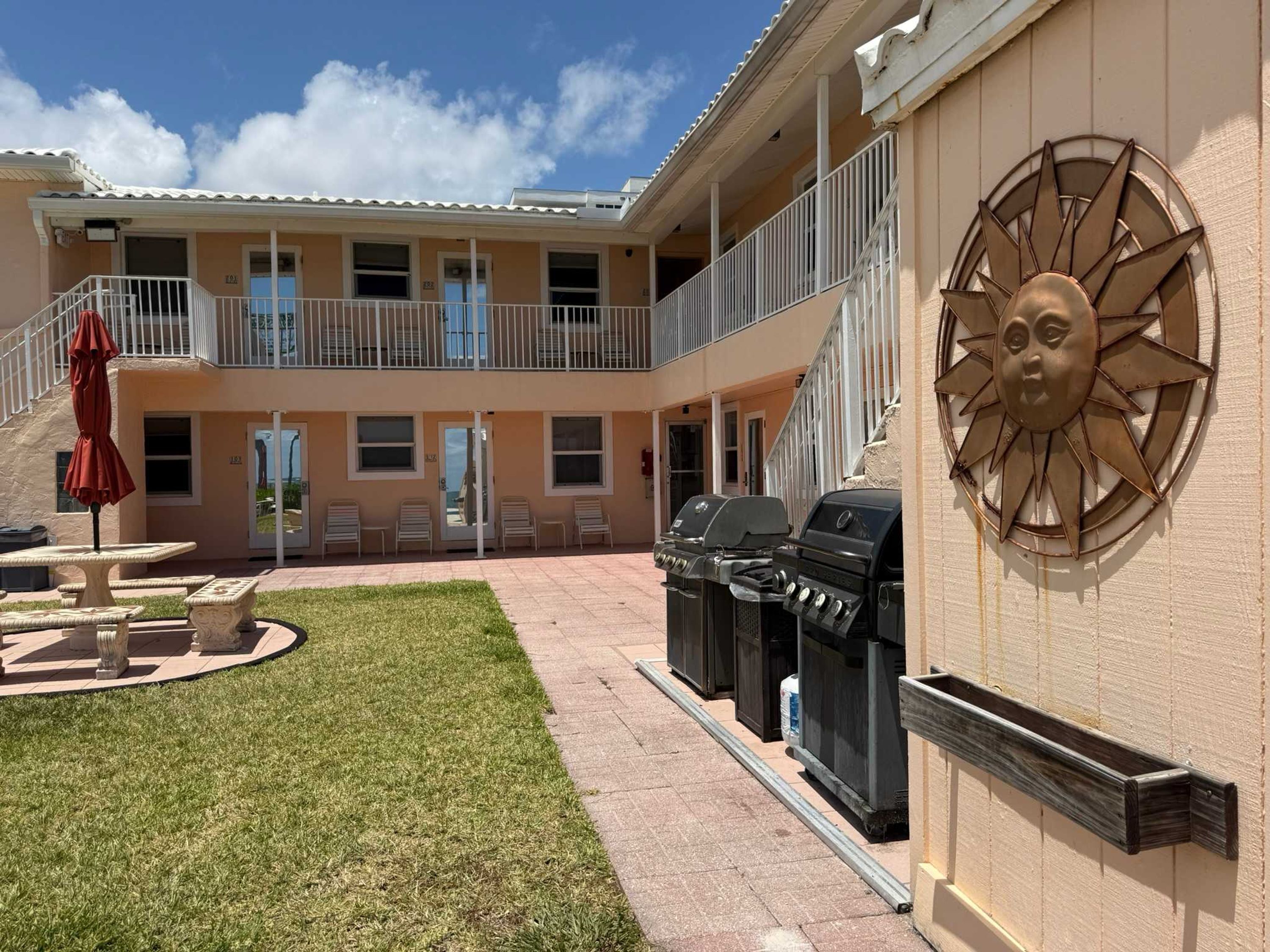 Un patio con una parrilla, mobiliario exterior y un adorno mural con forma de sol.