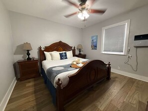 A bedroom with a wooden bed, two bedside tables with lamps, a ceiling fan, a window with blinds, and a painting on the wall. - Oceanfront Hidden Gem in Hollywood Beach (Hollywood)