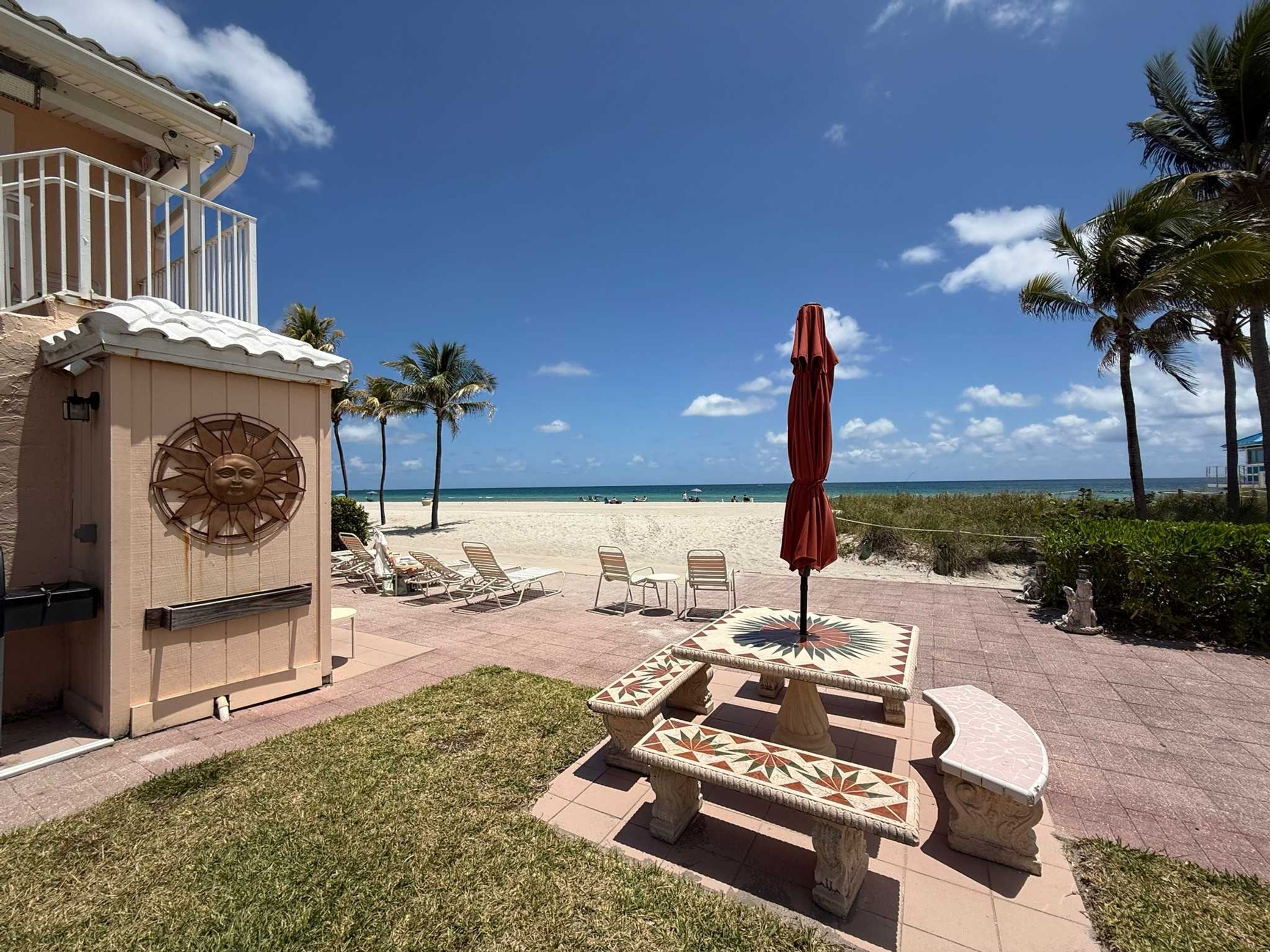 A patio with lounge chairs, a table, and an umbrella, overlooking a beach.