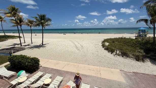 Una playa con sillas de descanso, palmeras y una torre de salvavidas.
