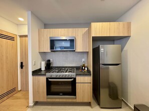 A compact kitchen with a built-in microwave, a stainless steel refrigerator, a gas stove, and wooden cabinetry. - w Upscale Loft w Balcony in Roma Norte (Mexico City)