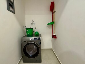 A compact laundry area with a front-loading washing machine, a green bucket, and a red mop on a wall-mounted rack. - w Upscale Loft w Balcony in Roma Norte (Mexico City)