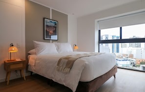 A modern hotel room with a large bed, two bedside lamps, a city view, and a framed picture on the wall. - w Upscale 2BR w Balcony View in Miraflores (Lima)