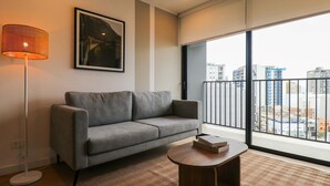 Een moderne woonkamer met een grijze bank, een vloerlamp, een ronde salontafel en een groot raam met uitzicht op de stad.