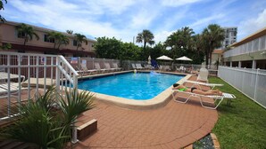 Une piscine avec des chaises longues, un espace délimité par une clôture et un bâtiment en arrière-plan.