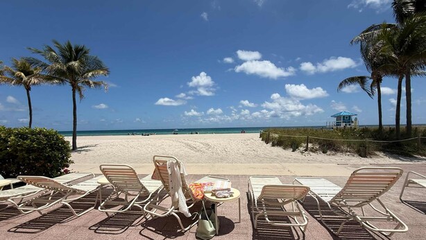 Un espace de détente aménagé au bord de la plage, avec des chaises longues, une petite table et une vue sur la plage et l’océan.