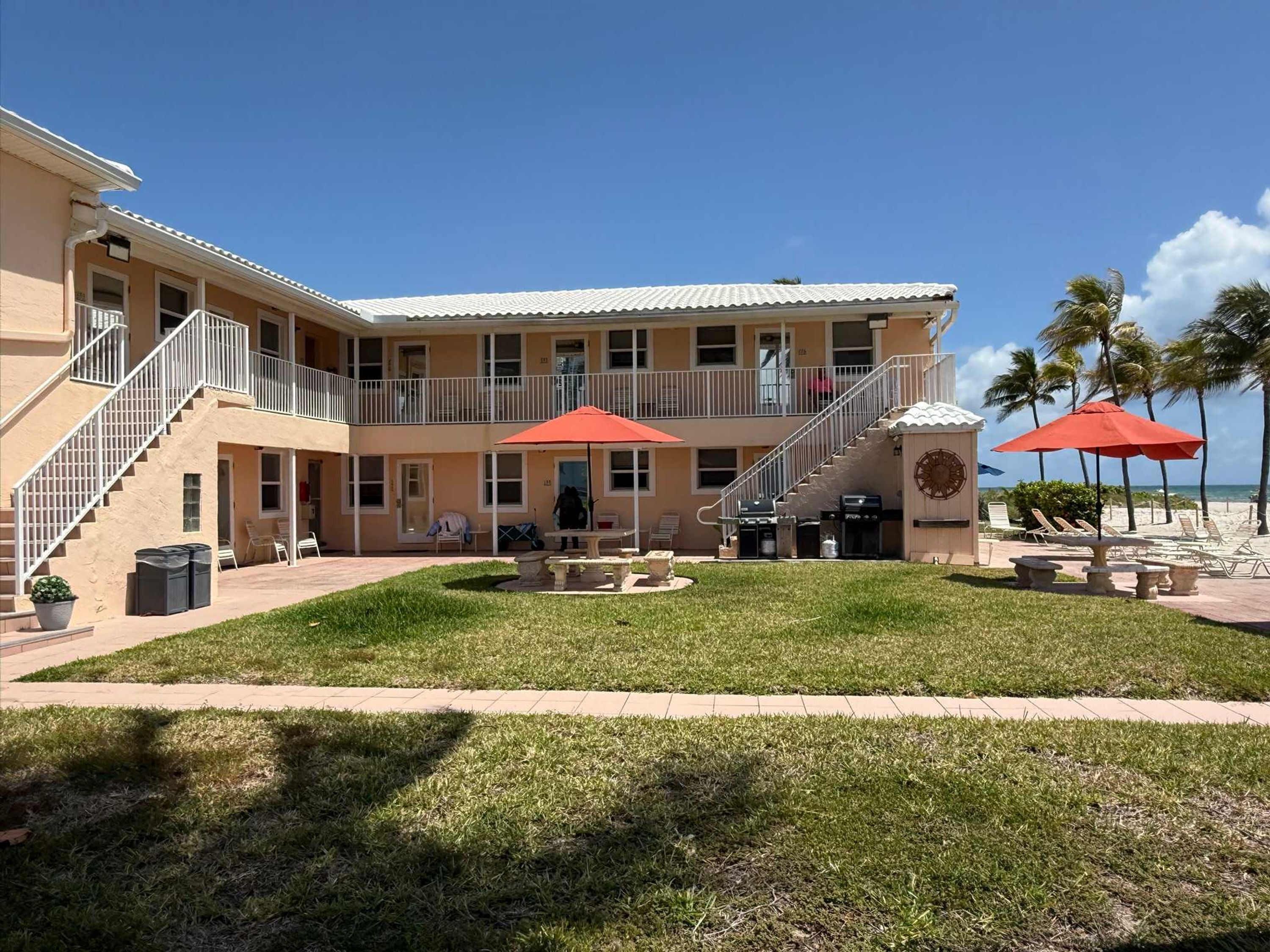 A two-story building with a covered patio, outdoor seating, and a view of the beach.