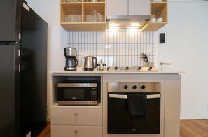 Eine kleine Küche mit einem schwarzen Kühlschrank, einer Mikrowelle, einem Backofen, einer Kaffeemaschine und Holzregalen über der Arbeitsfläche.