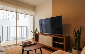 Ein modernes Wohnzimmer mit Flachbildfernseher, einer Couch, einem Couchtisch und einem Balkon mit Geländer.