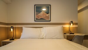 Habitación de hotel con cama, dos lámparas de noche, un escritorio con silla y un cuadro en la pared.