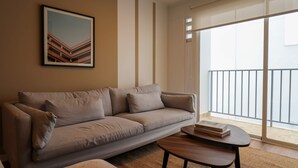 Una sala de estar con sofá, una mesa de centro, un cuadro enmarcado en la pared y un balcón con barandilla.