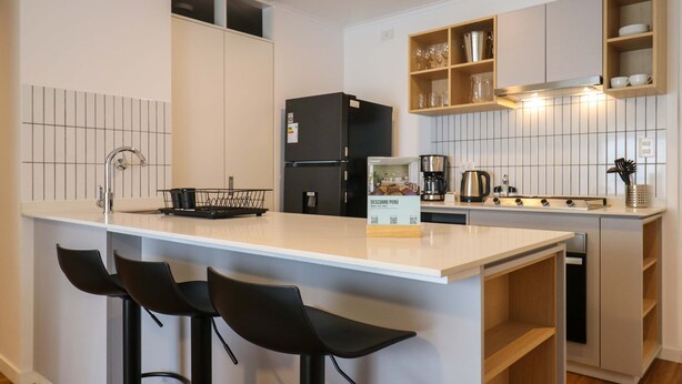 Una cocina moderna con una isla central, taburetes de bar, un refrigerador, una cafetera y estantes de madera.