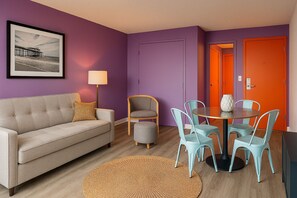 Ein Wohnzimmer mit einer Couch, Sesseln, einem Tisch, einer Lampe und einem gerahmten Bild an der Wand.