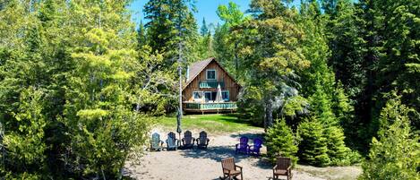 Eine Hütte mit Terrasse, umgeben von Bäumen, mit Gartenmöbeln und einer Feuerstelle.