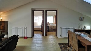 A room with a sloped ceiling, a radiator, a bed, a table with a lamp, and a chair.