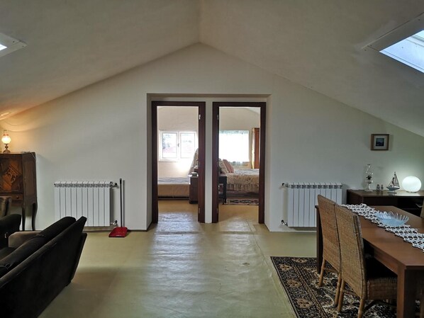 A room with a sloped ceiling, a radiator, a bed, a table with a lamp, and a chair.