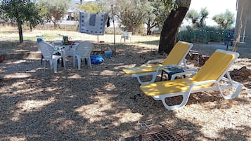 An outdoor seating area with white plastic chairs and a table, surrounded by trees and a fence.