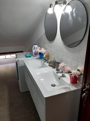 Et moderne badeværelse med hvid vask, to spejle, toilet og bruseområde.
