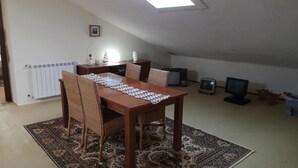 A dining area with a table, chairs, a patterned rug, a radiator, and a TV.