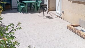 Un cortile con tavolo e sedie, un barbecue e una porta che dà su un ambiente interno.