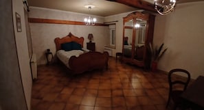 A bedroom with a wooden bed, a mirror, a nightstand, and a chandelier. - Spacious, peaceful village house. (Escamps)