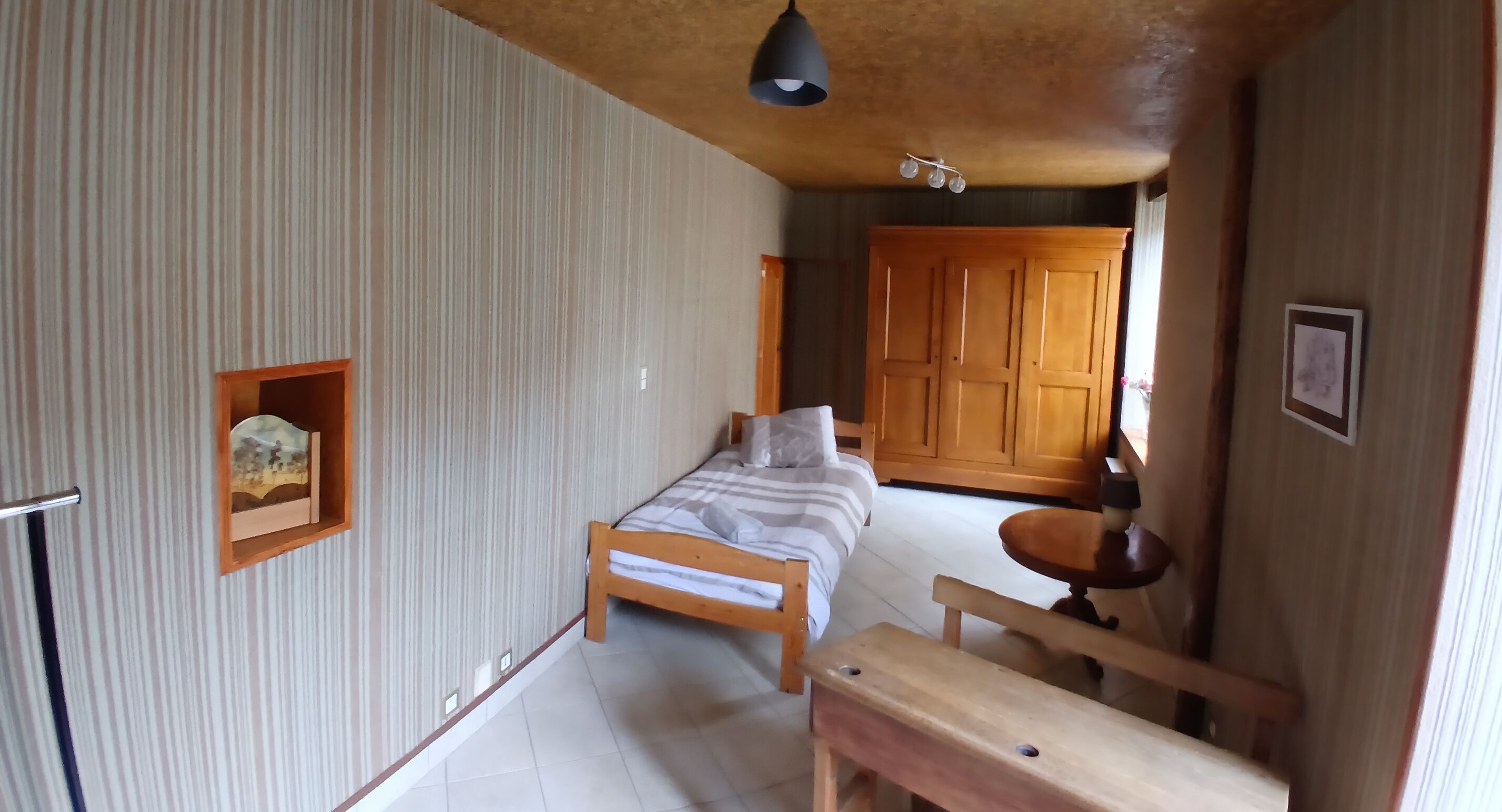 A bedroom with a bed, bedside table, wooden wardrobe, and a small shelf with a picture.
