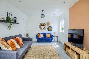 A living room with a grey sofa, a blue sofa, a TV on a wooden stand, and a ceiling fan.