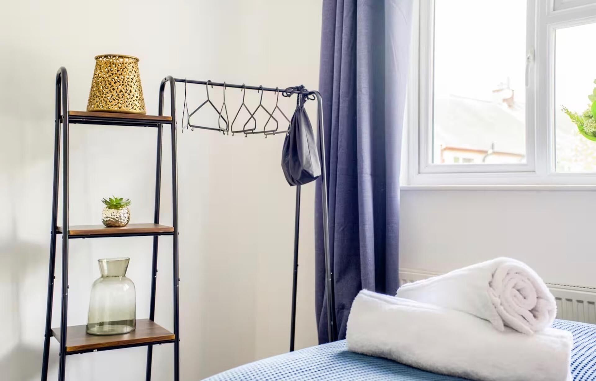 A neatly organized room with a bed, a shelf with decorative items, and a window with curtains.