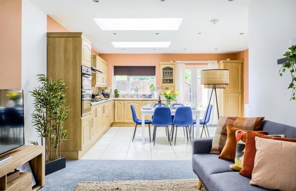 A modern kitchen with a dining area, a sofa, and a TV.