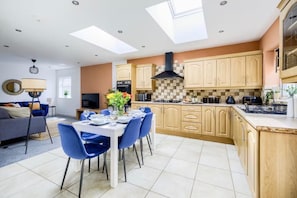 A modern kitchen with a dining area, featuring a central island, wooden cabinets, and a large window.