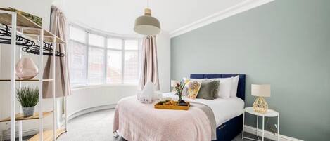 Une chambre à coucher avec un lit, une table de chevet, une lampe et une fenêtre avec des rideaux.