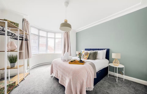 A bedroom with a bed, bedside table, lamp, and a window with curtains.