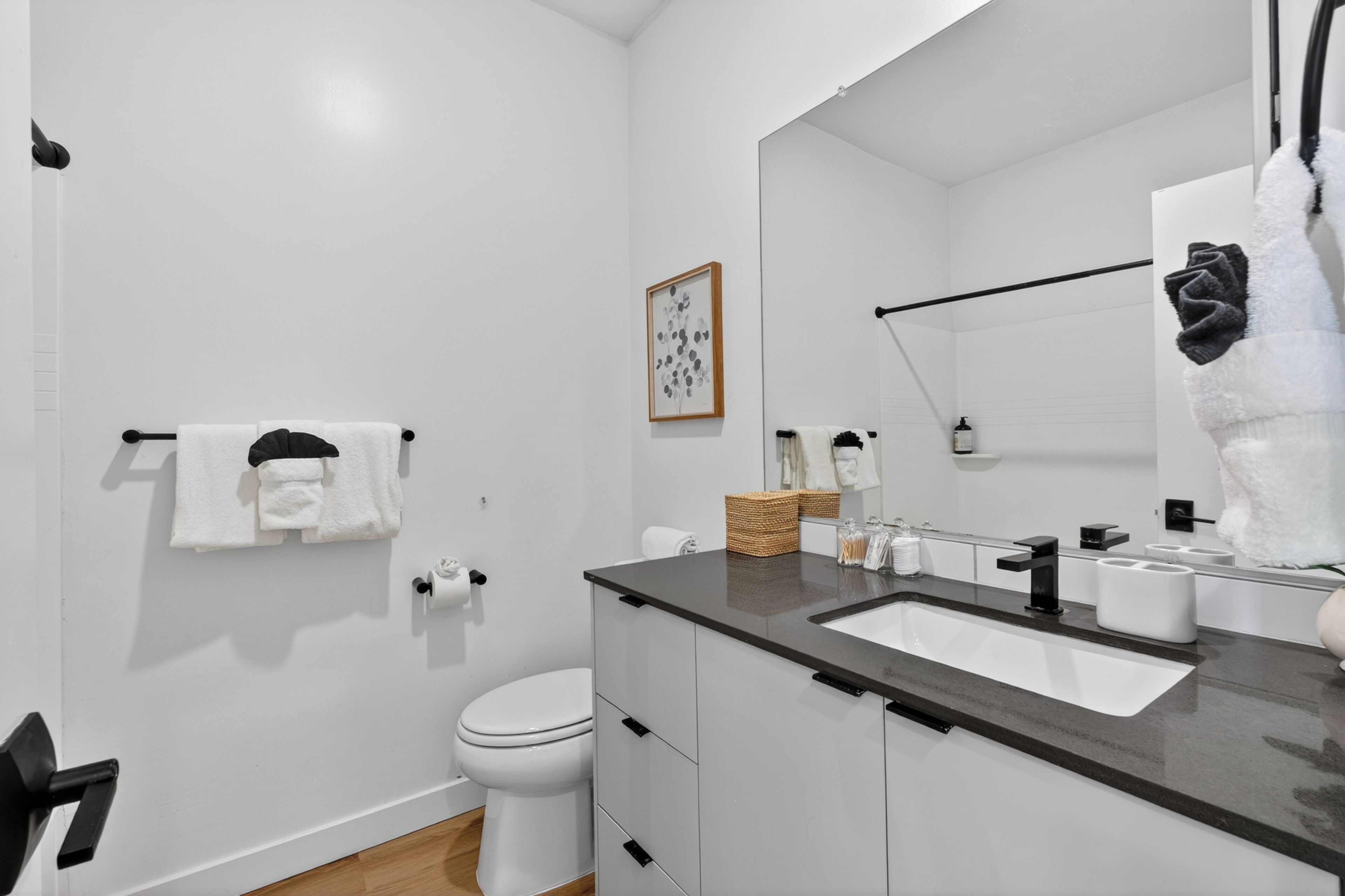 A modern bathroom with a white toilet, a large mirror, a dark countertop sink, and a towel rack.