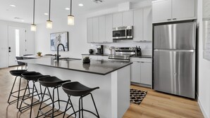 A modern kitchen with stainless steel appliances, a central island with bar stools, and pendant lighting. - Copper Sky Townhome - Pool & Gym (Phoenix)