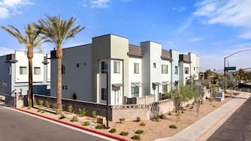 A modern multi-story residential building with a flat roof, large windows, and a landscaped front yard with palm trees and shrubs.