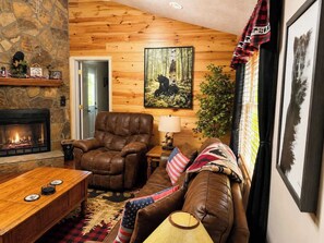 Ein gemütliches Wohnzimmer mit Kamin, Ledermöbeln und Wandkunst mit Waldmotiv.