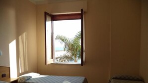 Una habitación con dos camas, un ventanal con vista a palmeras y una puerta.