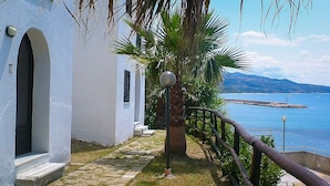 Un edificio costero con un camino de piedra, una palmera y vistas al mar y a las montañas.