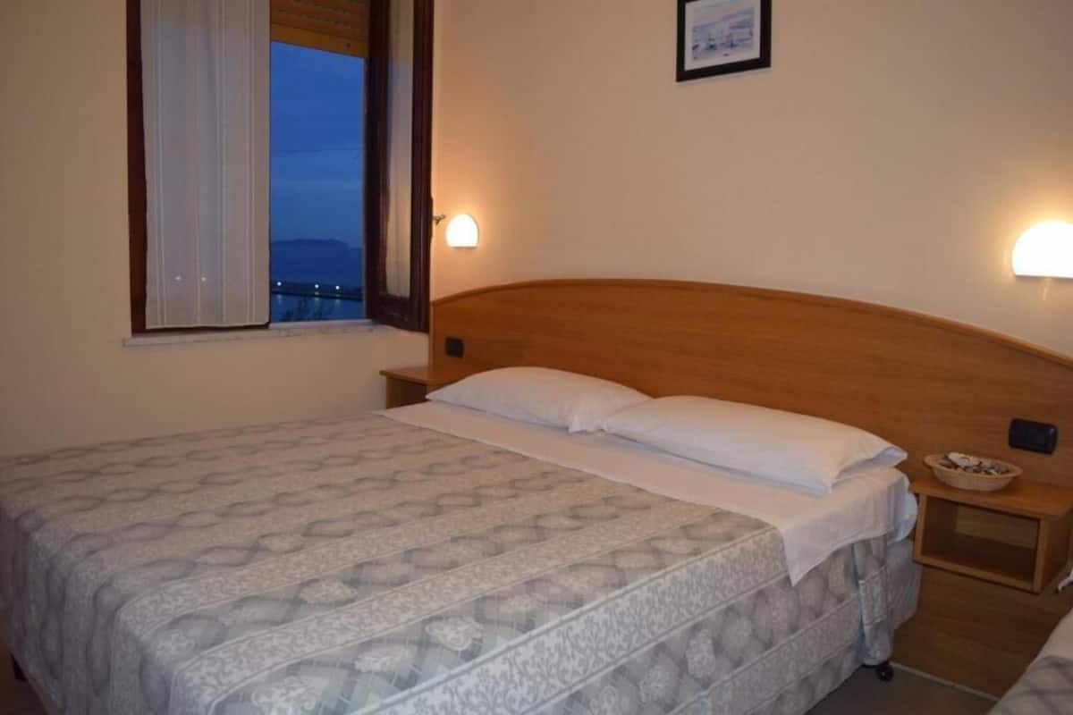 A single bed with a patterned bedspread, a wooden headboard, bedside tables with lamps, and a window with curtains.