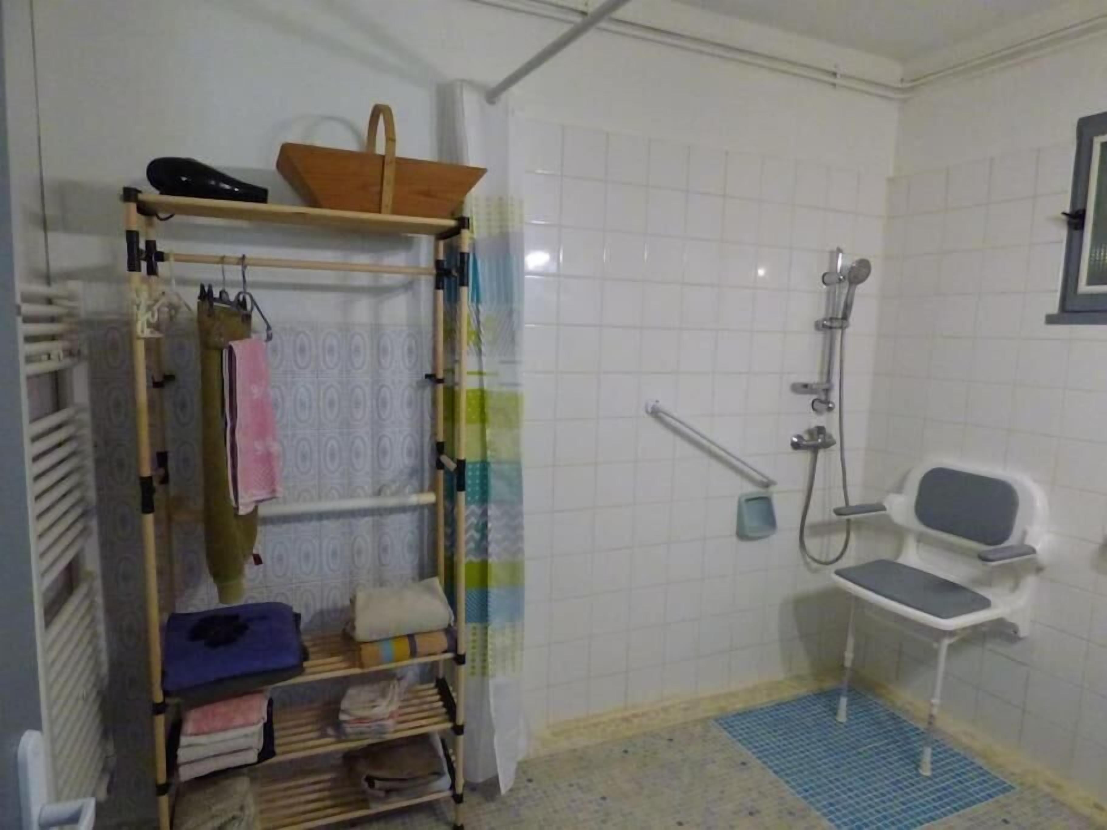 A bathroom with a shower, a toilet, a shelf with towels, and a small shelf with a basket.