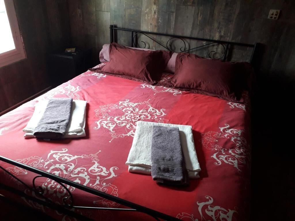 A bed with a red and white patterned bedspread, two pillows, and two folded towels.
