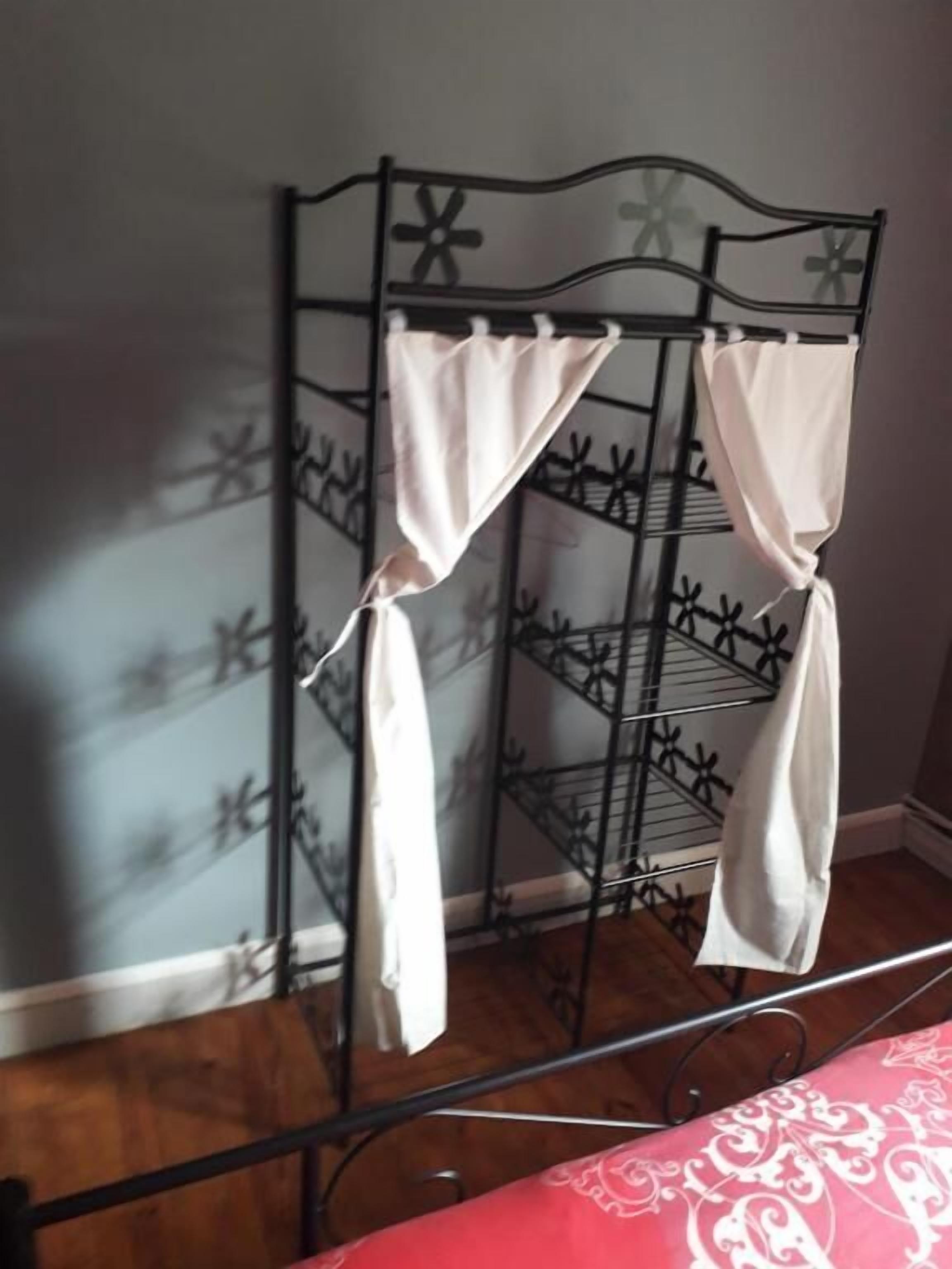 Una estantería metálica con cortinas blancas, suelo de madera y una colcha estampada.