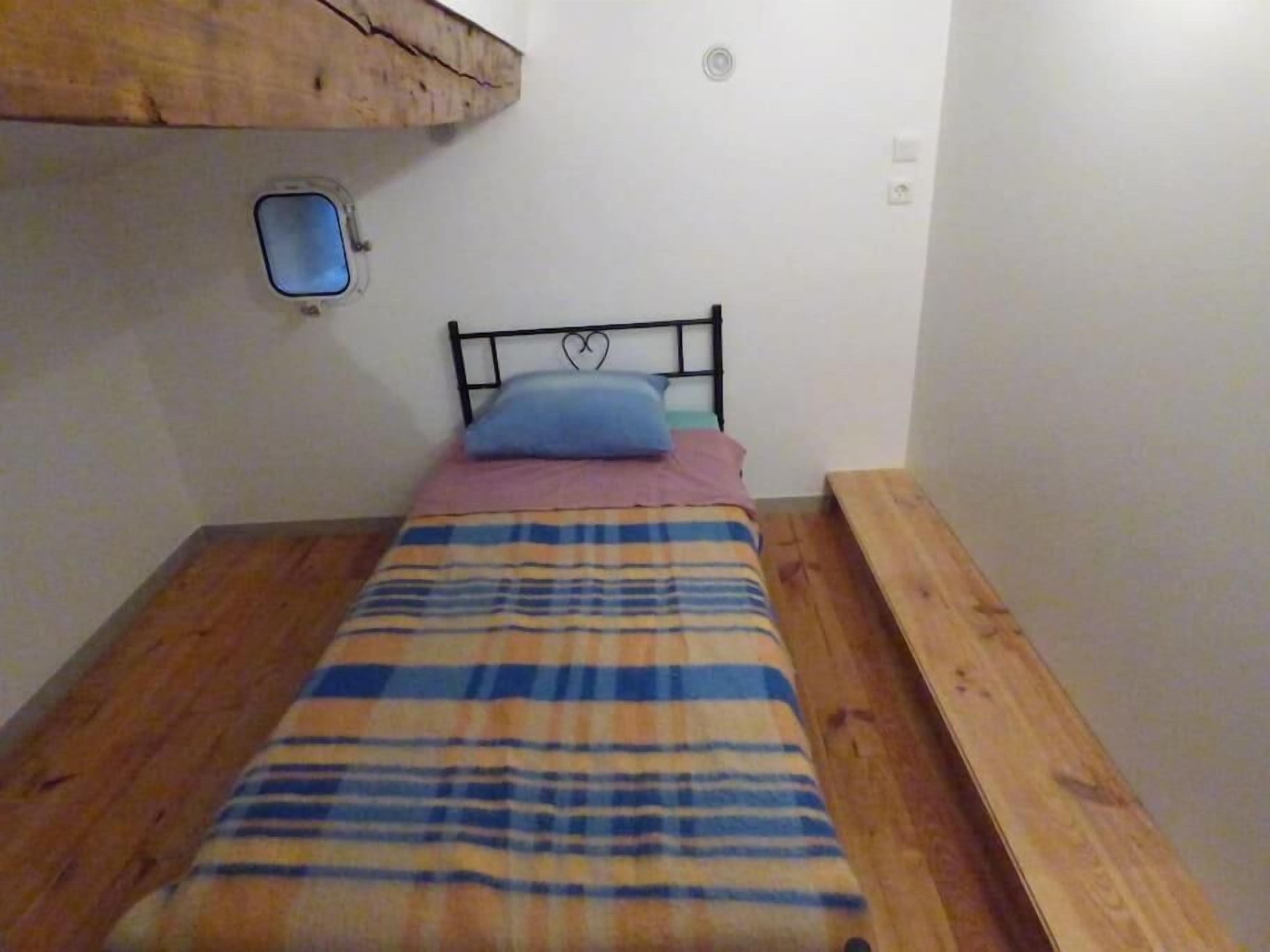 A single bed with a plaid blanket, a blue pillow, and a wooden headboard.