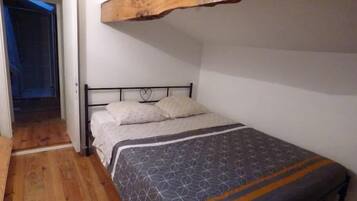Una cama individual con estructura metálica, cabecera de madera y colcha estampada.